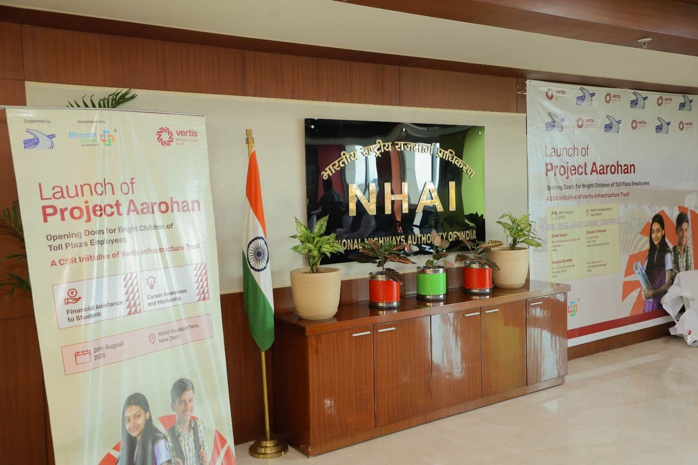 Two Project Aarohan launch banners flanking a gold NHAI wall sign, beside an Indian flag and potted plants on a wooden cabinet