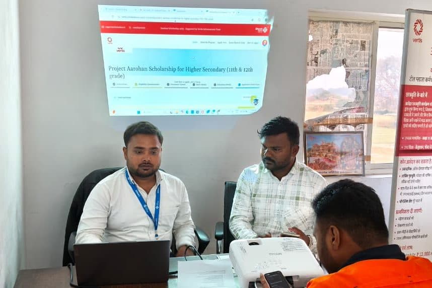 Two staff members at a desk with a laptop, the Aarohan application page projected on the wall behind them
