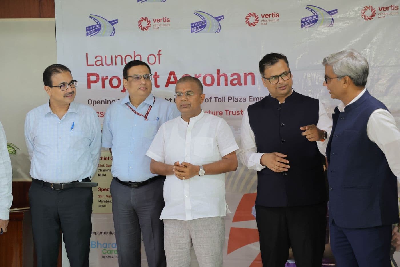 Five officials standing and talking in front of the Project Aarohan launch banner